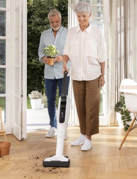 Zwei Personen in hellem Raum, eine mit kabellosem Staubsauger, die andere hält eine Pflanze.